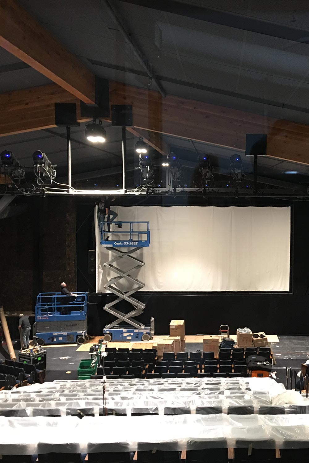 Workers on lifts installing lighting and screen in theater with covered seating