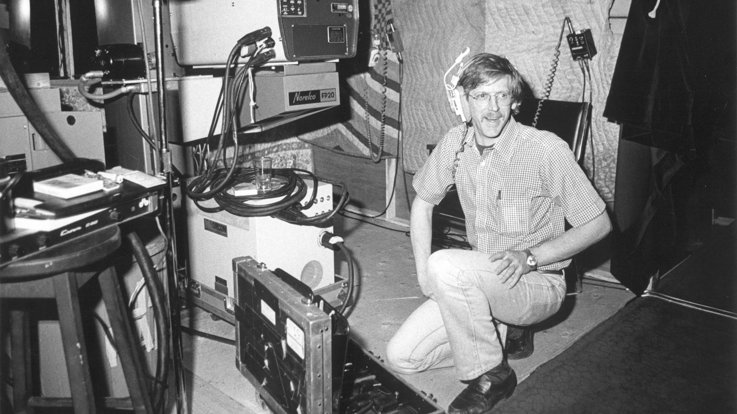 Man kneeling with headphones next to a Norelco FP20 projector setup