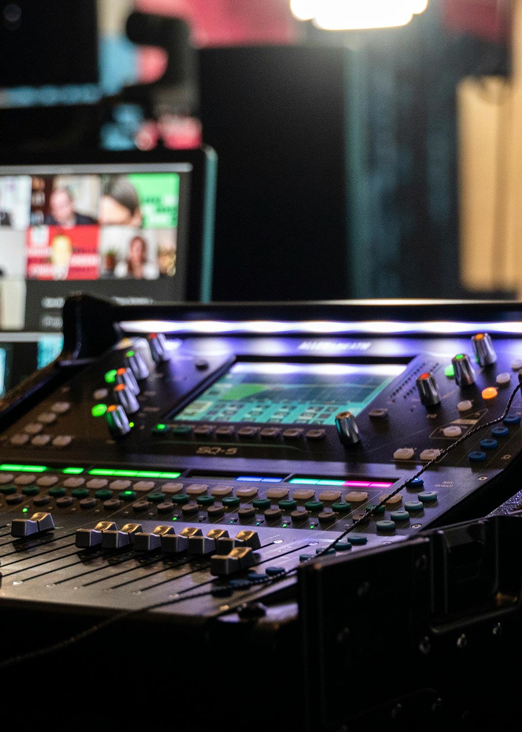 A close-up of an illuminated digital audio mixing console with various control knobs and screens.