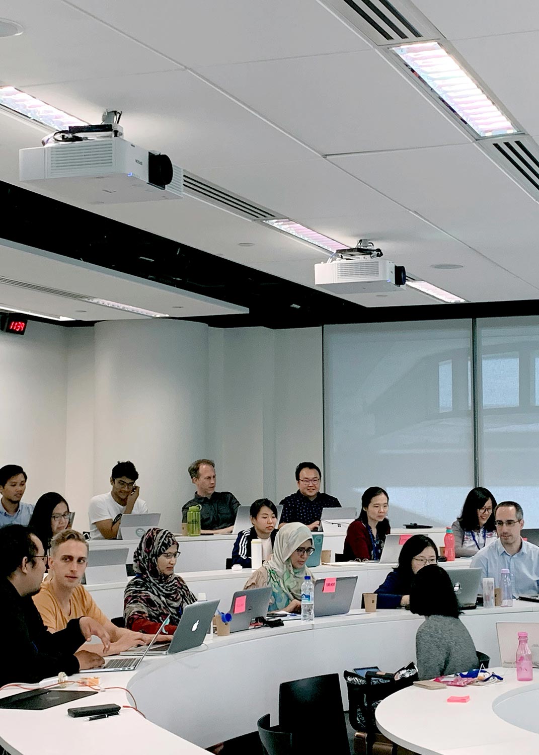 A classroom with students using laptops, featuring ceiling-mounted projectors and a modern design.