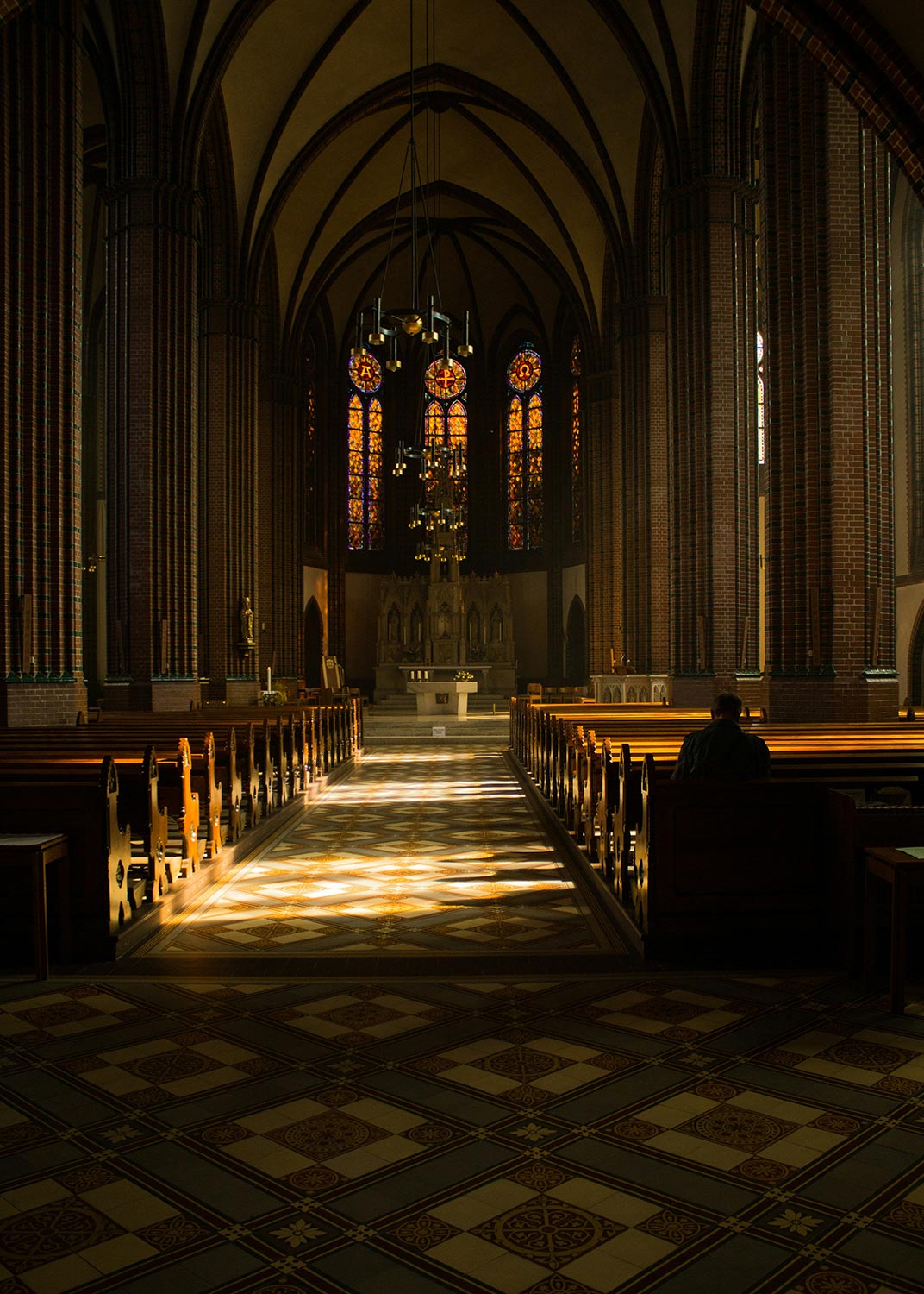A grand church interior with high ceilings, wooden pews, and colorful stained glass windows casting light patterns on the floor.