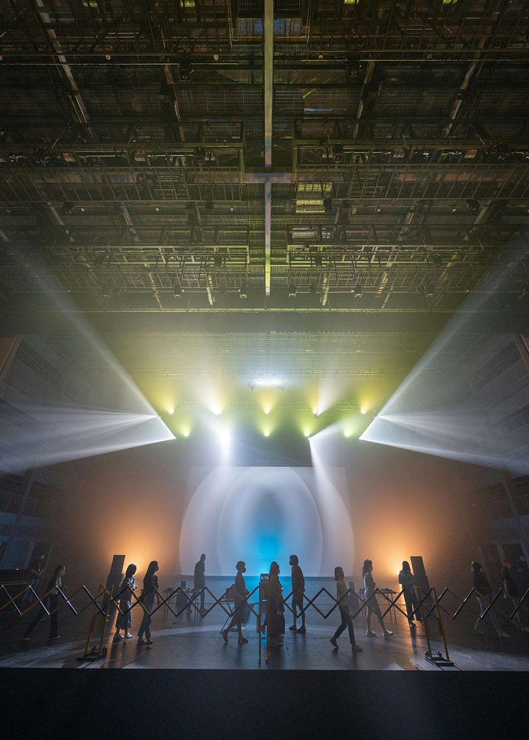 A group of people walking towards a bright stage with dramatic lighting and fog effects.