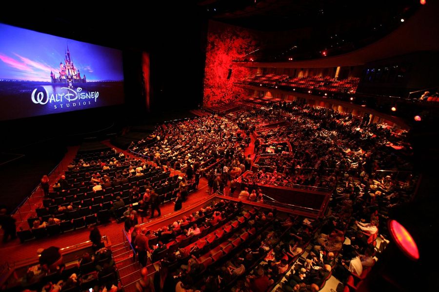 Full audience in red-lit theater with Disney logo onscreen