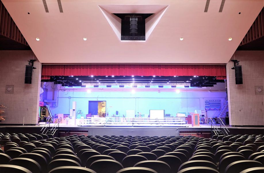 Empty auditorium facing a lit-up stage under red curtain