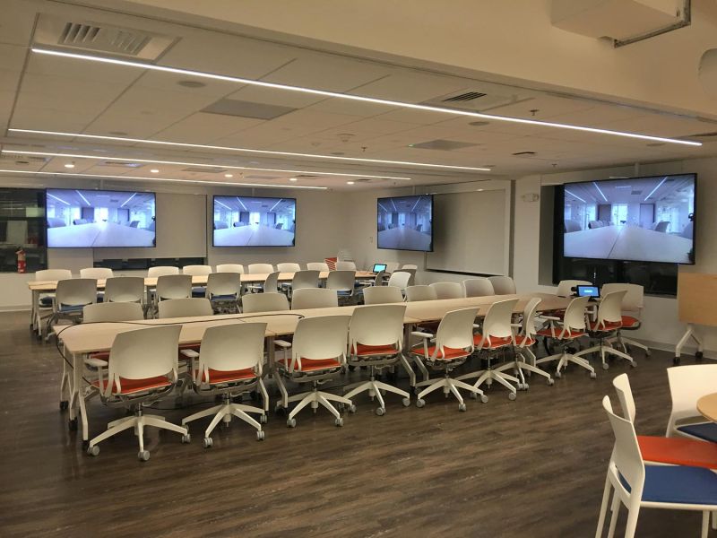 Modern classroom with white chairs, wood floors, and large screens on walls