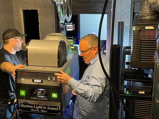 Two men working with a Boston Light & Sound projector in a control room