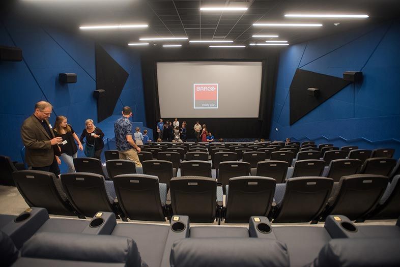 Blue-walled theater with large screen and people entering the auditorium