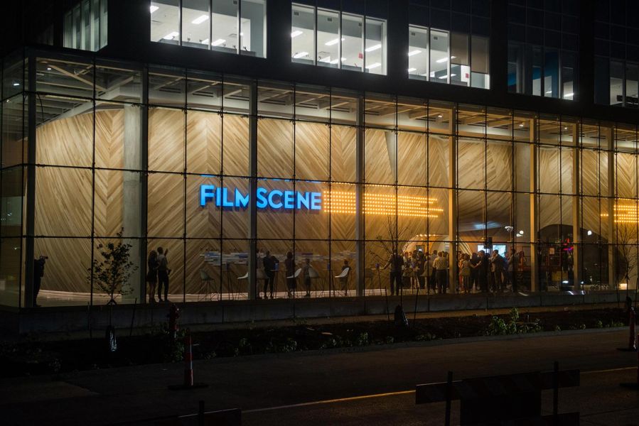 Glass-fronted building with illuminated Film Scene sign and people inside