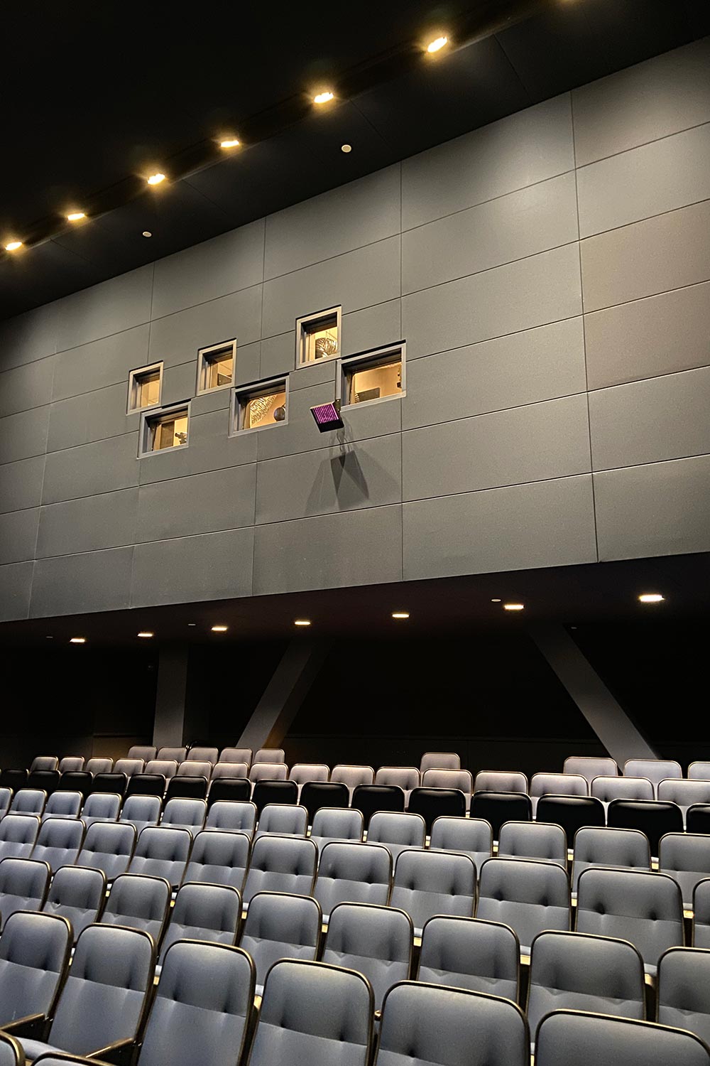 View of theater seating with projection booth windows on a dark paneled wall