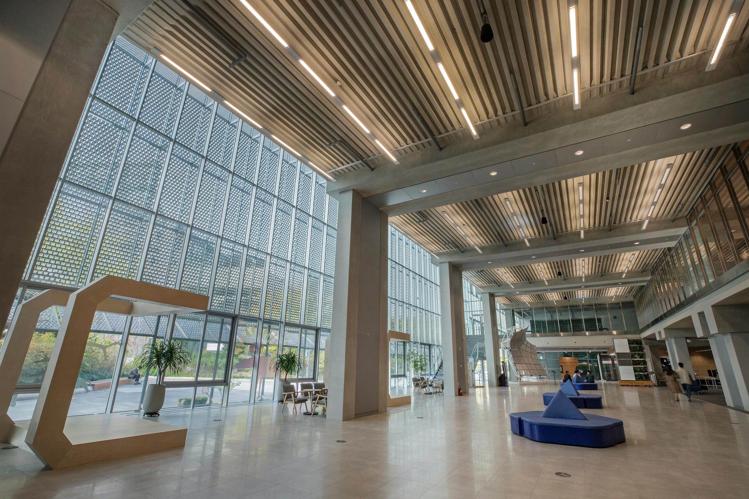 A spacious modern lobby with large glass windows, wooden ceiling slats, and stylish seating.