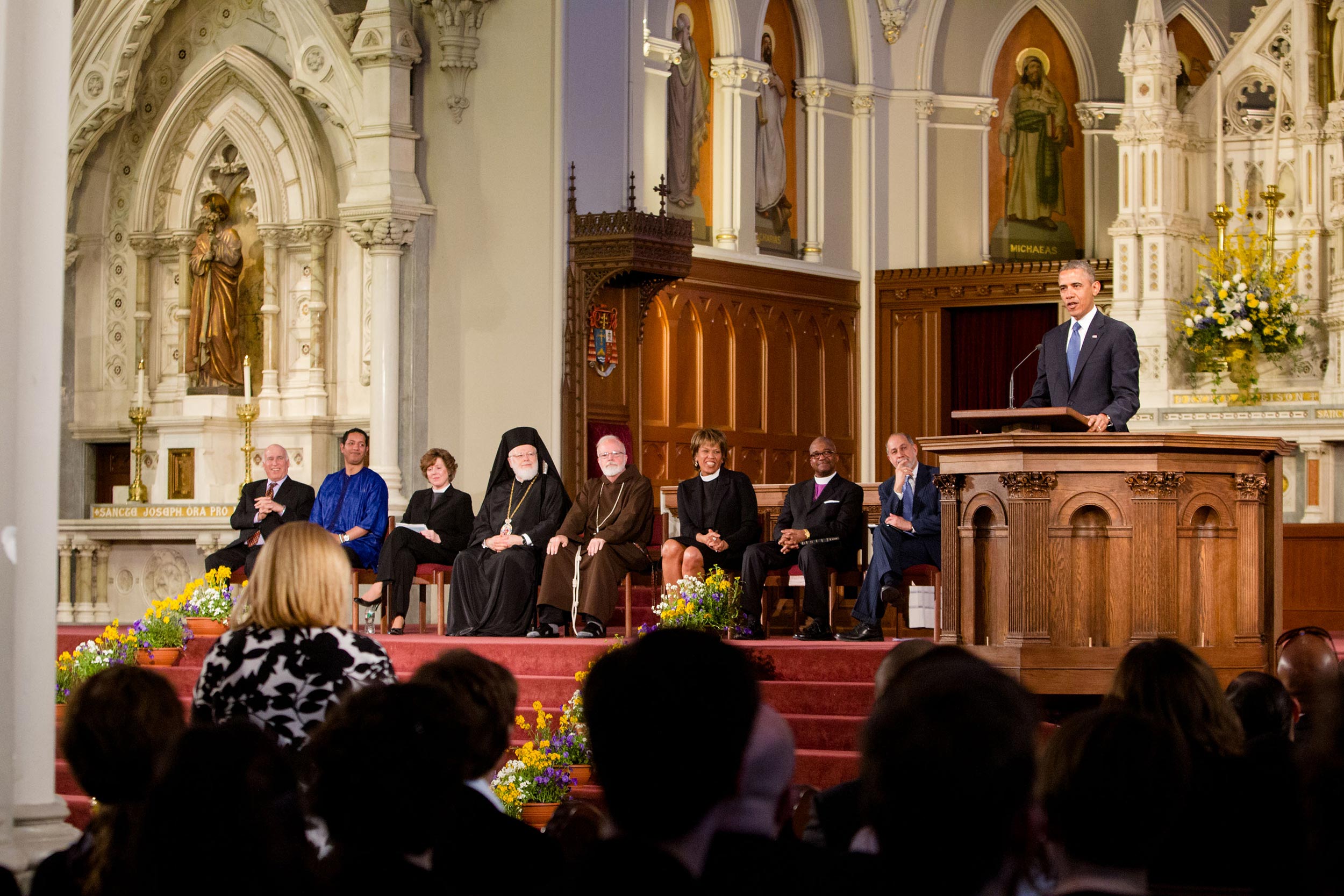 A church service with a speaker addressing a diverse panel and congregation in a grand cathedral.