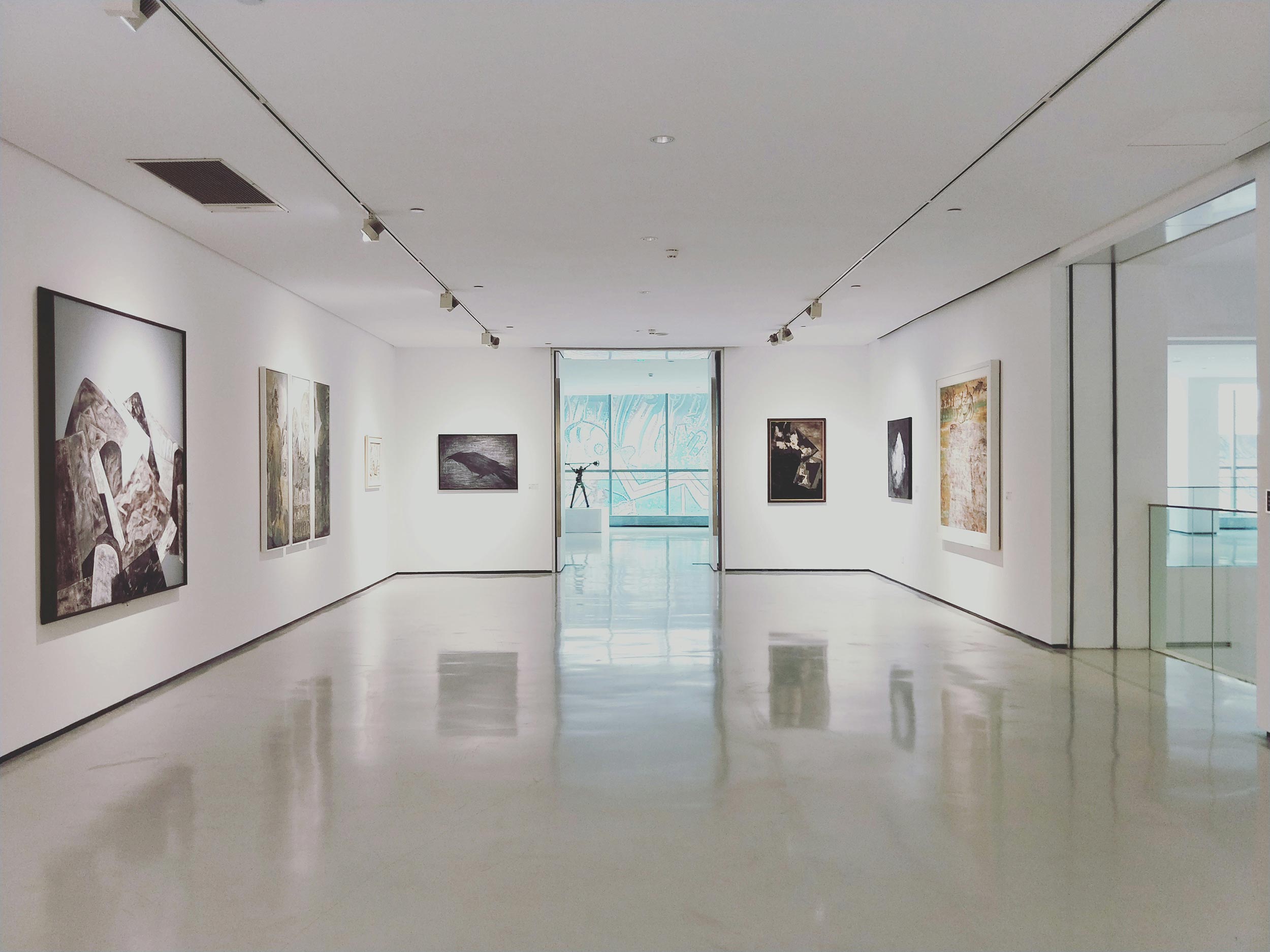 A modern art gallery with white walls, minimalist lighting, and framed artwork on display.