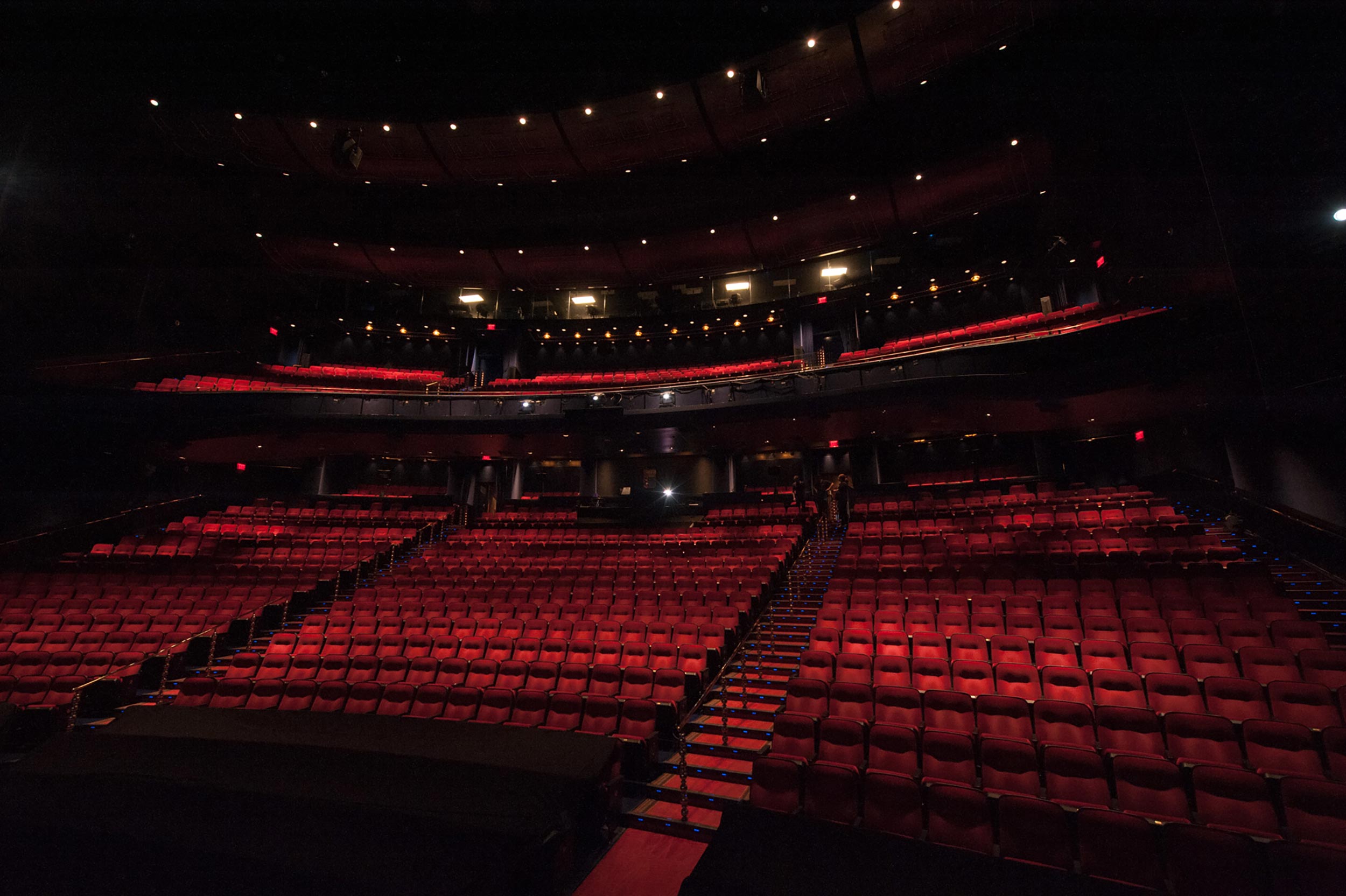 A dimly lit theater with rows of red seats facing a dark stage.
