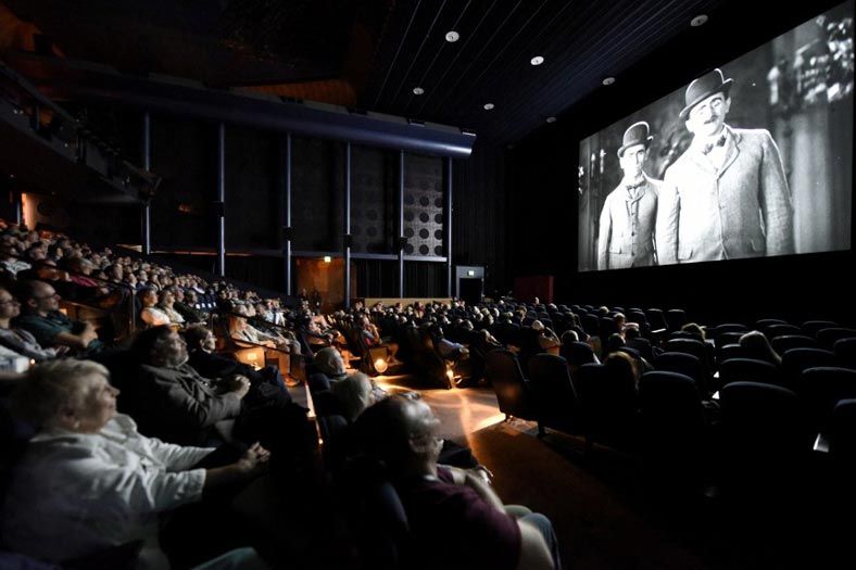 Packed theater watching a black-and-white film on a large screen