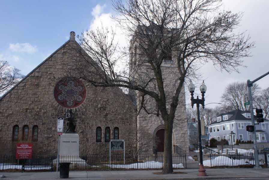 Exterior of stone church with statue of Theodore Parker and bare trees