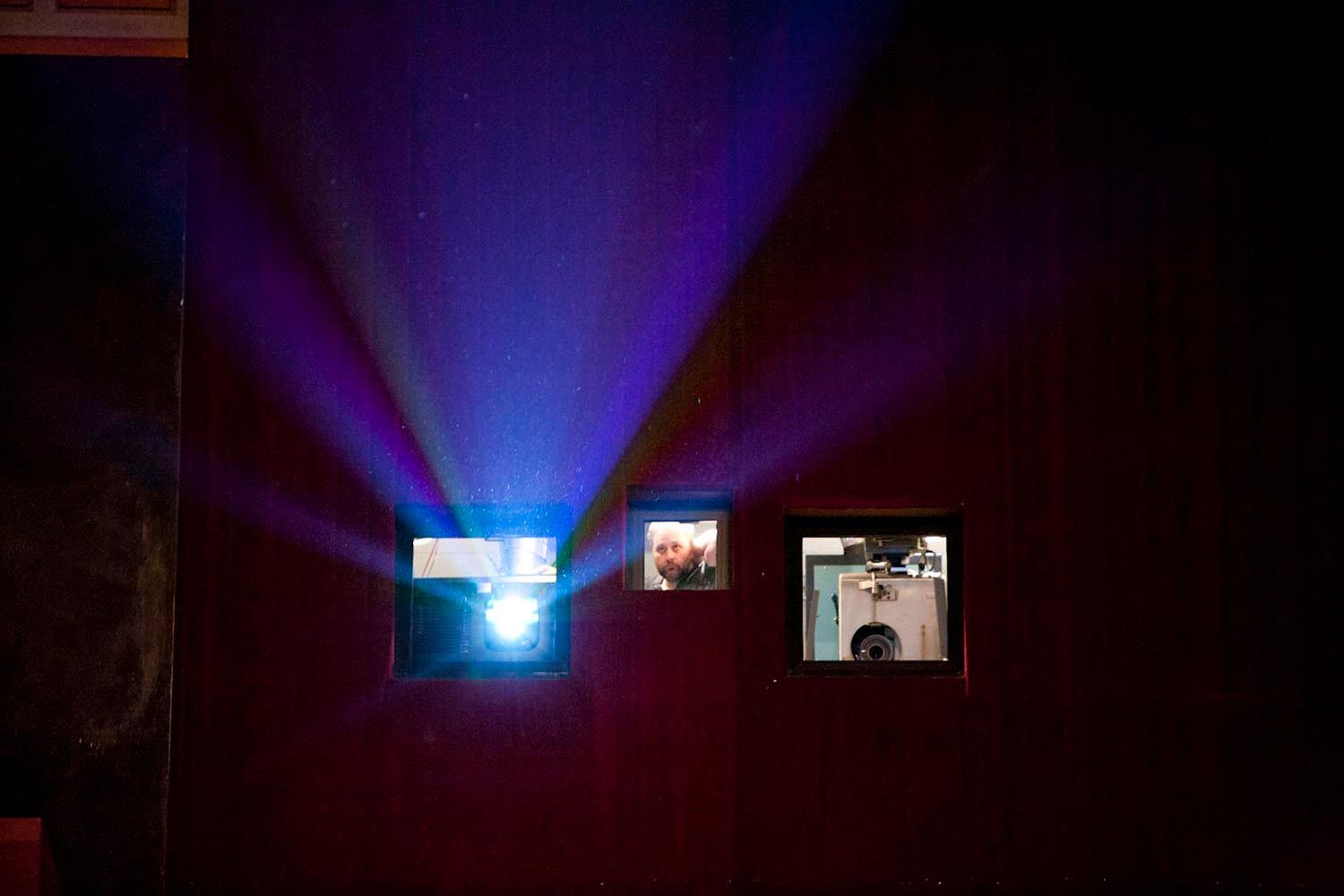 Light from a projector shining through a small booth window with a man inside
