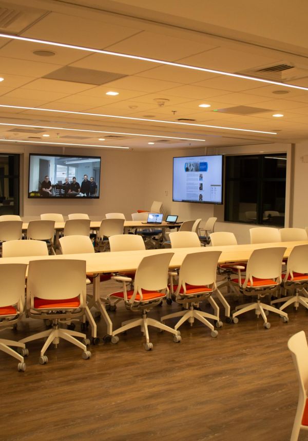 Modern classroom with white chairs, wood floors, and large screens on walls